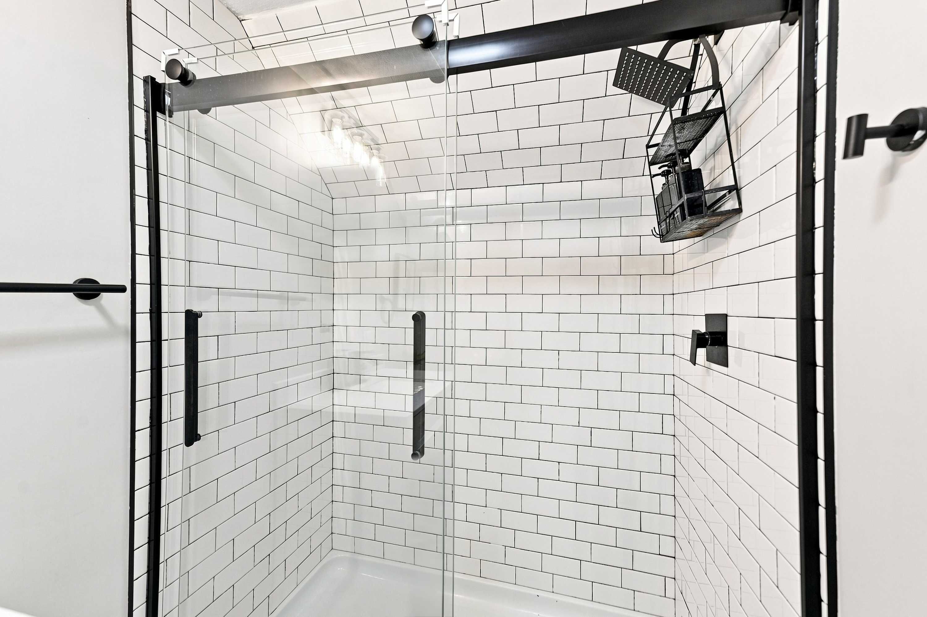 Une douche avec des carreaux blancs et un cadre en métal noir.