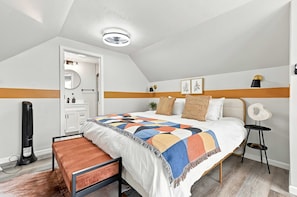 A bedroom with a bed, a bedside table, a chair, a heater, a ceiling fan, and a door.