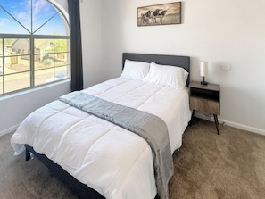Une chambre à coucher avec un lit, une table de chevet, une lampe, une fenêtre et un tableau au mur.