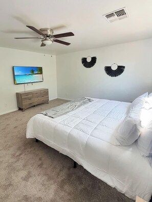 Ein Schlafzimmer mit Bett, Deckenventilator, Fernseher und Wandlüfter.