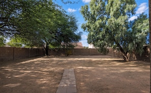 Un espace extérieur doté d’un chemin pavé, entouré d’un mur de briques et d’arbres.