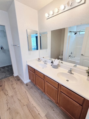 Une salle de bain avec un meuble-lavabo à deux vasques, des armoires en bois, un grand miroir et un espace douche.