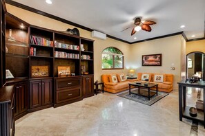 A spacious living room with a large bookshelf, a sofa set, a coffee table, and a ceiling fan. - Jungle Pool Villa - 5BR Gated Playacar Hideaway (Playa del Carmen)