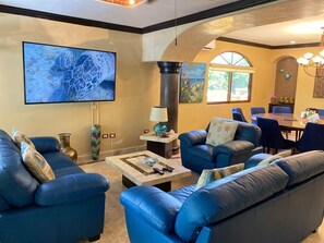 A living room with blue leather sofas, a flat-screen TV, and a dining area with a table and chairs. - Jungle Pool Villa - 5BR Gated Playacar Hideaway (Playa del Carmen)