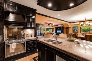 A modern kitchen with a stove, sink, and dark cabinetry. - Jungle Pool Villa - 5BR Gated Playacar Hideaway (Playa del Carmen)