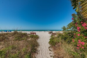 Un camí de sorra que porta a l'oceà, amb gandules i ombrel·les de platja.