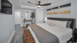 Ein Schlafzimmer mit einem Bett, einer Bank, einem Deckenventilator, einem Schminktisch und Wandbildern.