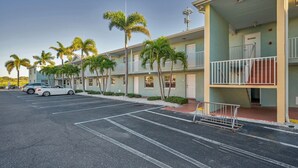 Ein mehrstöckiges Hotel mit Parkplatz, Palmen und einem weißen Auto.