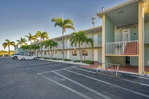 Ein mehrstöckiges Hotel mit Parkplatz, Palmen und einem weißen Auto.