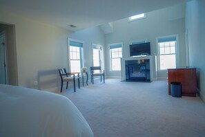 A spacious bedroom with a large bed, a fireplace, and a TV.