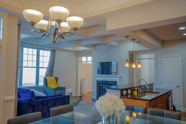 A spacious living room with a fireplace, a dining area with a glass table, and a kitchen with a sink and countertop.