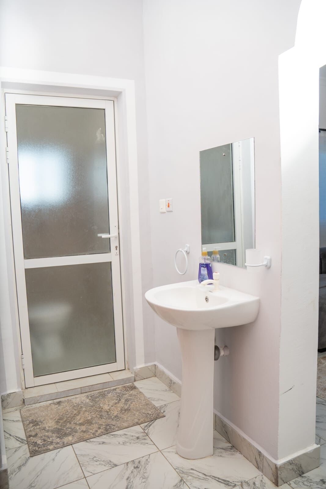Casa de banho com lavatório branco, porta de vidro e espelho na parede.