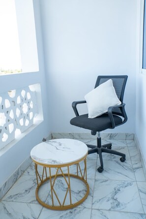 Ein kleiner Balkon mit weißem Marmorboden, einem schwarzen Bürostuhl mit weißem Kissen und einem runden Holztisch.