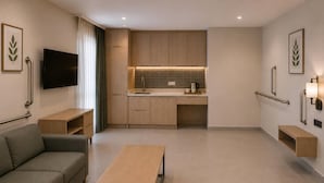 A modern hotel room with a sofa, a small table, a TV, a kitchenette, and a bathroom with grab bars. - Ramada Resort By Wyndham Datca (Datca)