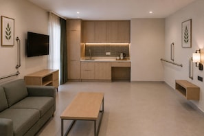 A modern hotel room with a sofa, a small table, a TV, a kitchenette, and a bathroom with grab bars. - Ramada Resort By Wyndham Datca (Datca)