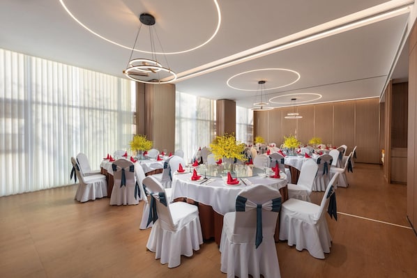A banquet hall with round tables, white chairs, and yellow flowers.