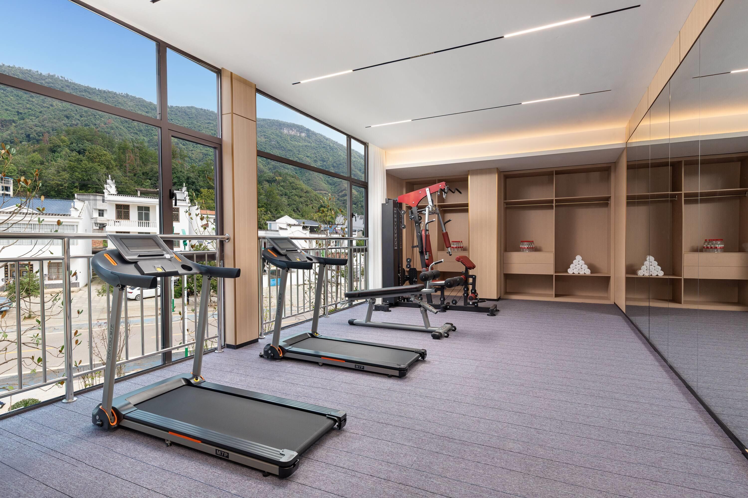 A gym with treadmills, weight machines, and a view of a mountainous landscape through large windows.