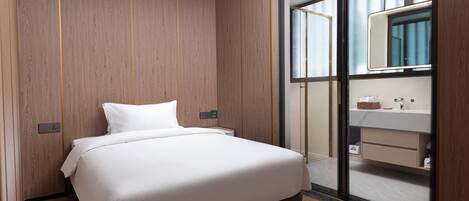 A modern bedroom with a wooden panel wall, a large bed, a nightstand, a bathroom with a mirror and sink, and a sliding glass door.