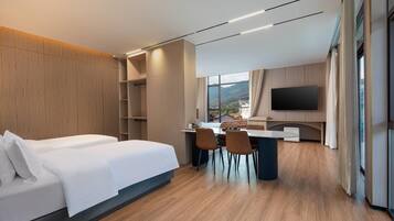 Une chambre d’hôtel moderne équipée d’un lit, d’un bureau, de chaises, d’un téléviseur à écran plat et offrant une vue sur l’extérieur.