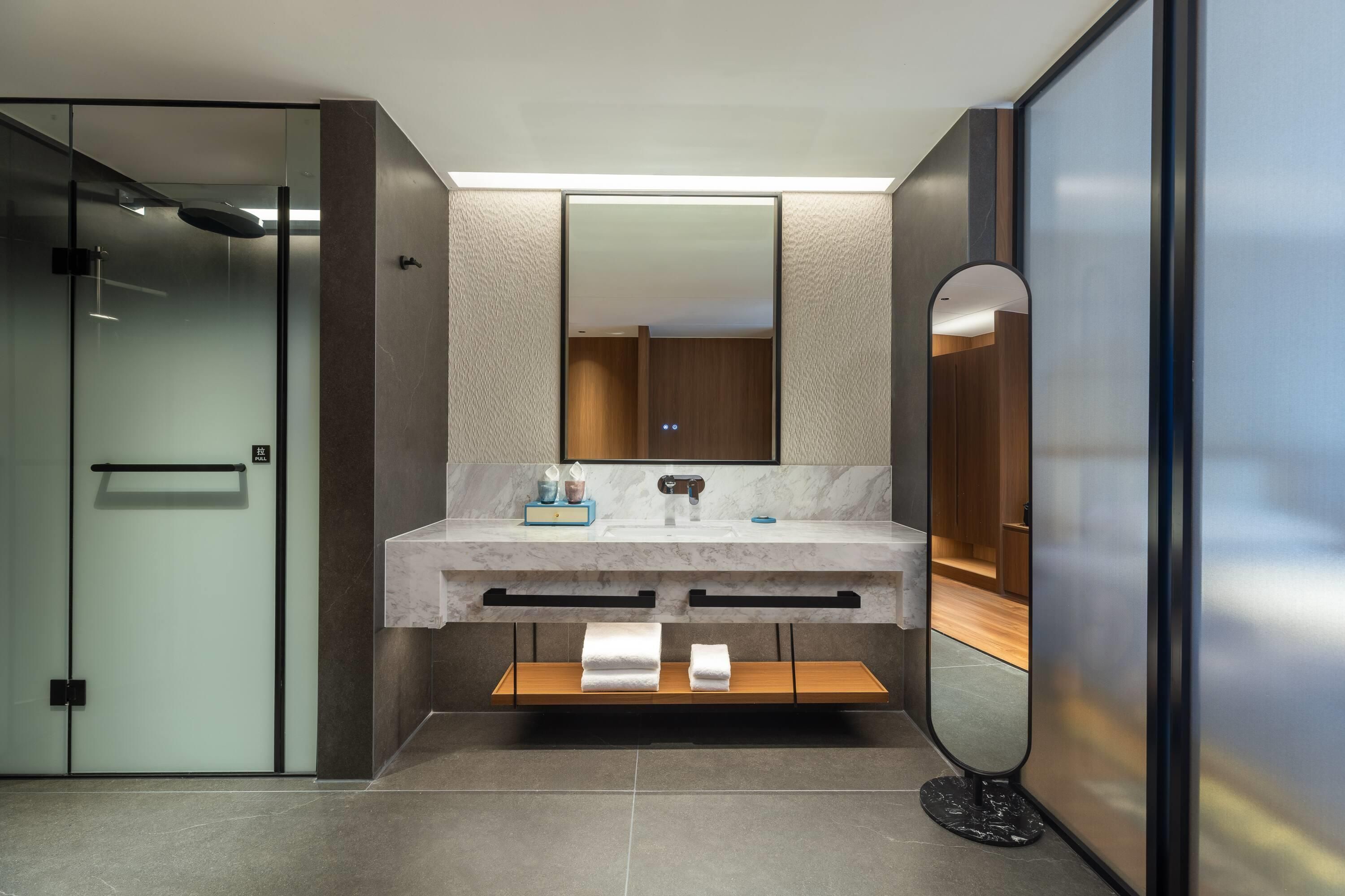 Un baño moderno con tocador de mármol, un espejo grande y cabina de ducha con paredes de vidrio.