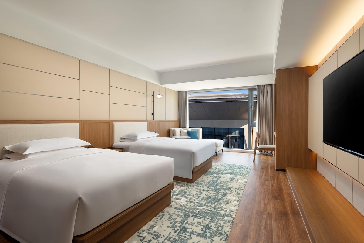 Quarto de hotel com duas camas, uma TV grande e vista para o exterior.