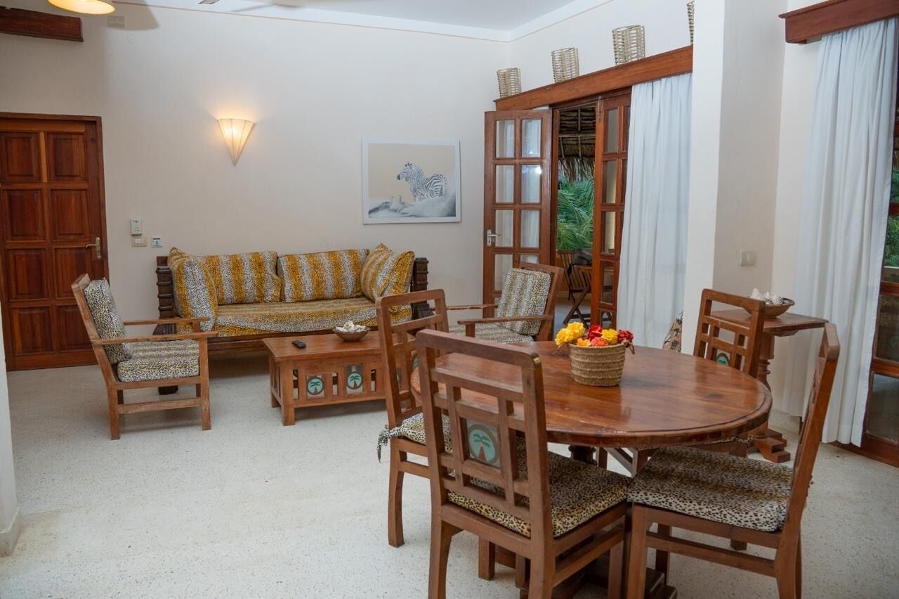 A dining area with a round wooden table, matching chairs, and a sofa with patterned cushions.