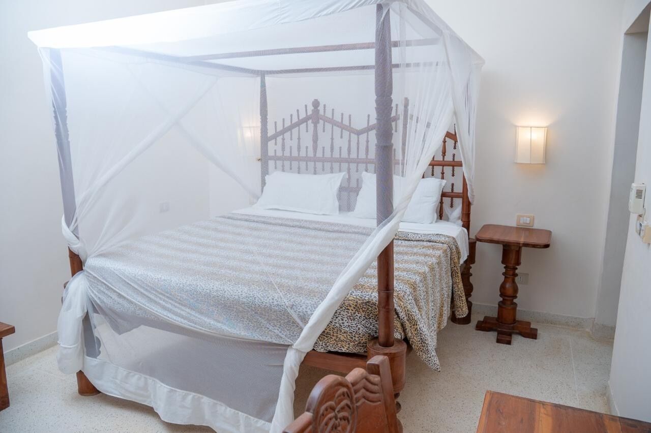 Un lit à baldaquin à quatre poteaux, avec une structure en bois et du linge de lit blanc, une table de chevet avec une lampe et un luminaire fixé au mur.
