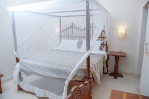A four-poster canopy bed with a wooden frame and white bedding, a bedside table with a lamp, and a wall-mounted light fixture.