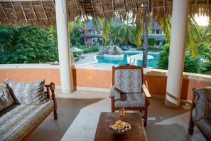 A covered outdoor seating area with a view of a swimming pool and resort buildings. - Tropical 2BR Malindi Condo | Pool & Balcony Views ❤️ (Malindi)