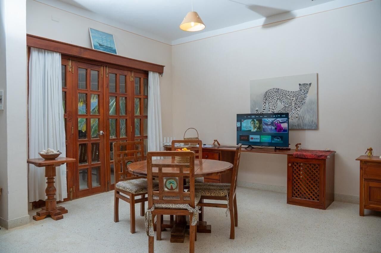 A dining area with a wooden table and chairs, a television, and a leopard print cushion.