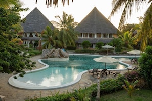 A resort with a swimming pool, lounge chairs, and thatched-roof buildings.