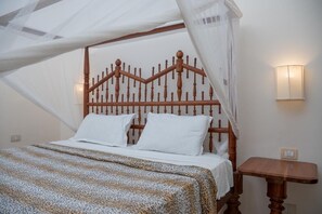 Uma cama com dossel, mesa de cabeceira e luminária fixada na parede.