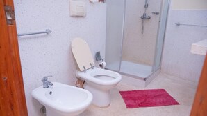 Een badkamer met twee toiletten, een douche, een bidet en een rode mat op de vloer.