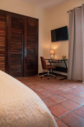 A hotel room with a bed, a desk with a chair, a television, and a window with curtains. - Step to the beach /Beautiful Penthouse + Private Terrace (San Juan)