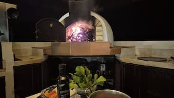 Une cuisine équipée d’un four à bois, d’un saladier rempli de légumes, d’une bouteille d’huile d’olive et d’ustensiles de cuisine.