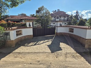 A gated entrance with a dirt path leading to a building with a tiled roof and a sign indicating a property name.