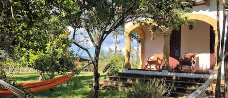 A hammock in a lush garden with a building featuring an arched entrance and outdoor seating.