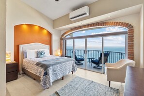 Una camera da letto con un letto grande, vista mare tramite una porta vetrata e un balcone con sedie.