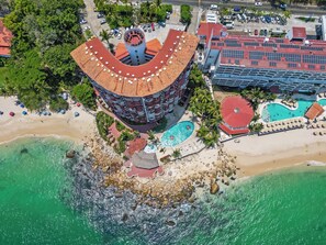 Vista aerea di un hotel con tetto curvo, piscina e spiaggia.