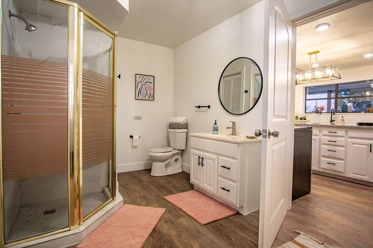 A bathroom with a glass shower enclosure, a toilet, and a sink with a mirror.
