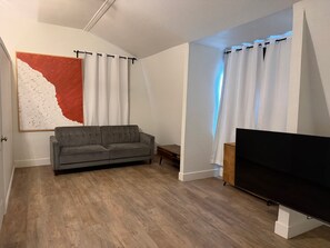A living room with a grey sofa, a flat-screen TV, a wooden coffee table, and a large abstract painting on the wall.