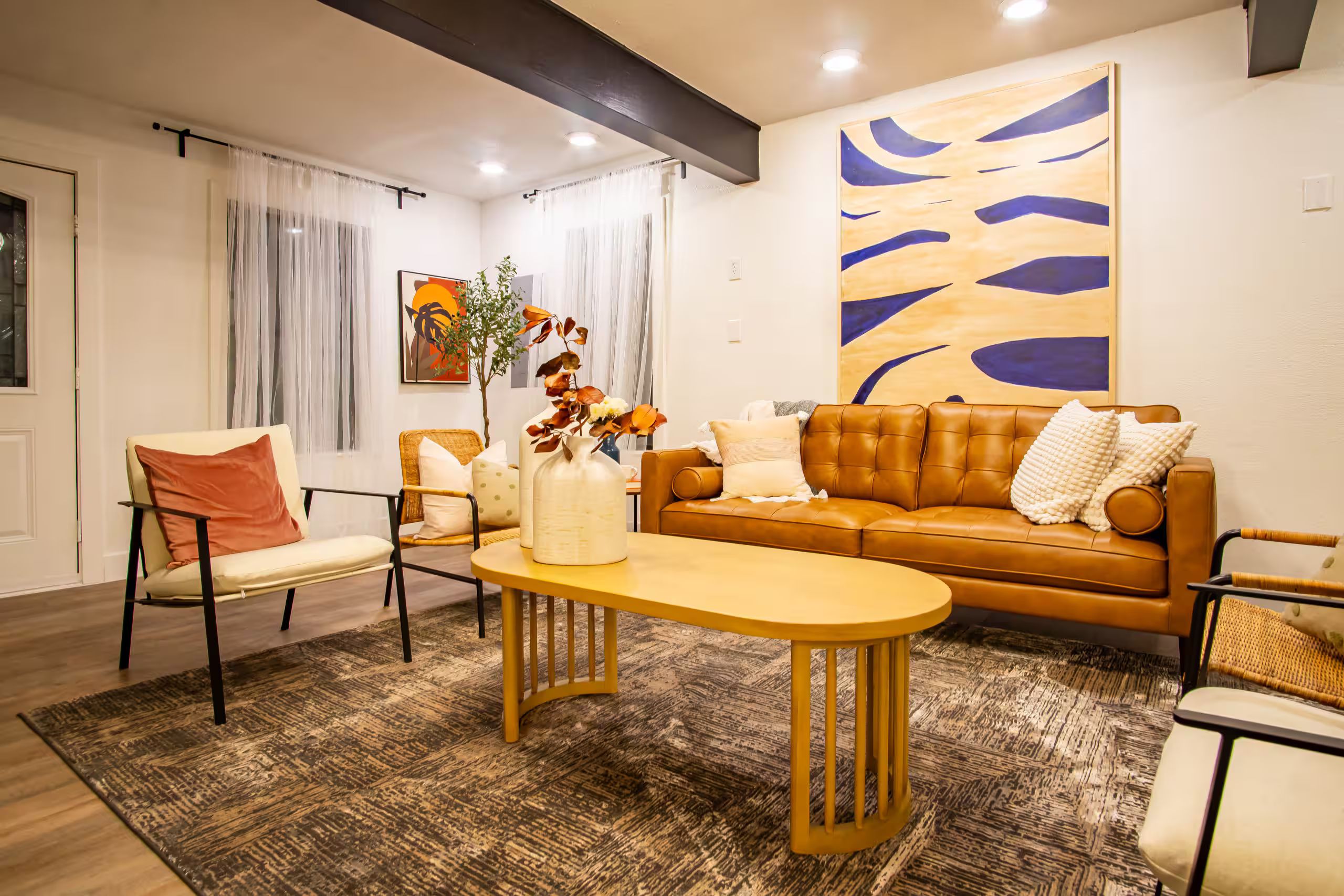 A modern living room with a brown leather sofa, a yellow coffee table, and a patterned rug.