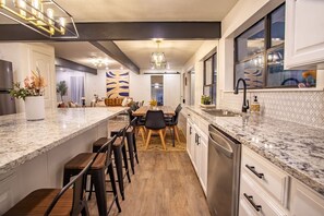 A modern kitchen with a central island, bar stools, and a dining area with a table and chairs.