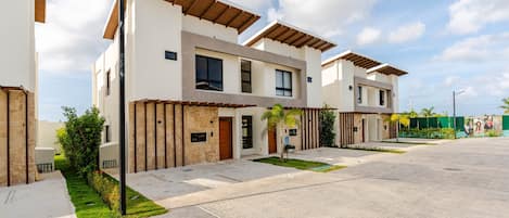 A modern residential building with a flat roof, large windows, and a paved driveway.