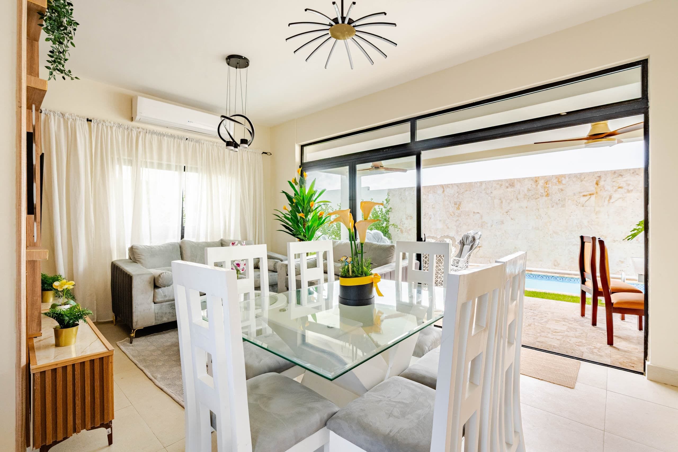 Ein modernes Wohnzimmer mit einem Glastisch, grauen Sofas und einem großen Fenster mit Blick auf einen Swimmingpool.
