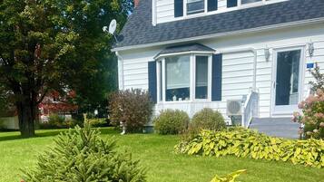 A two-story house with a well-maintained lawn, various shrubs, and a satellite dish.