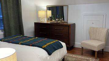 A bedroom with a bed, dresser, chair, and a large mirror.