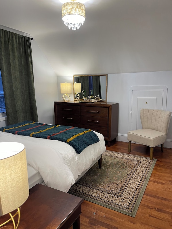 A bedroom with a bed, dresser, chair, and a large mirror.