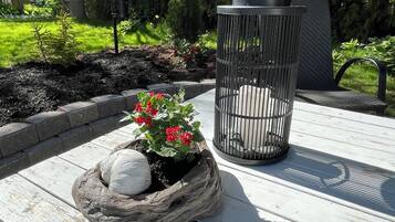 A wooden deck with a planter containing red flowers and white spherical stones, a metal trash can, and a bench.