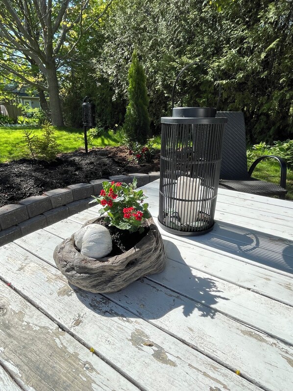 A wooden deck with a planter containing red flowers and white spherical stones, a metal trash can, and a bench.